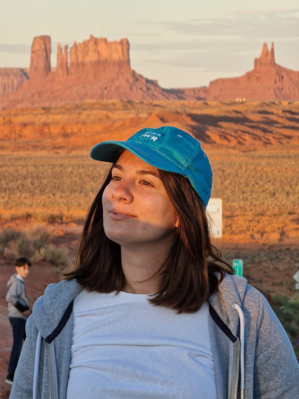 Alice Zilio travel designer, specializzata in viaggi negli Stati uniti, con un berretto blu osserva pensierosa il tramonto dal Forrest Gump Point, nella Monument Valley. Le formazioni rocciose rosse sullo sfondo creano un'atmosfera serena e naturale.
